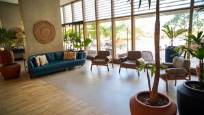 Un hall d’entrée spacieux, avec un canapé turquoise, plusieurs fauteuils, de grandes fenêtres et des plantes en pot.