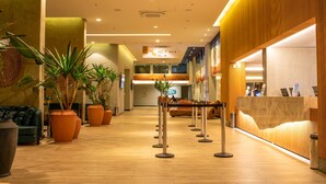 Un hall d’hôtel avec un comptoir d’accueil en bois, des plantes en pot et un espace salon.