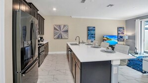 A modern kitchen with a large island, dark cabinetry, and a flat-screen TV. - Story Lake Town Home  With Pool (Kissimmee)