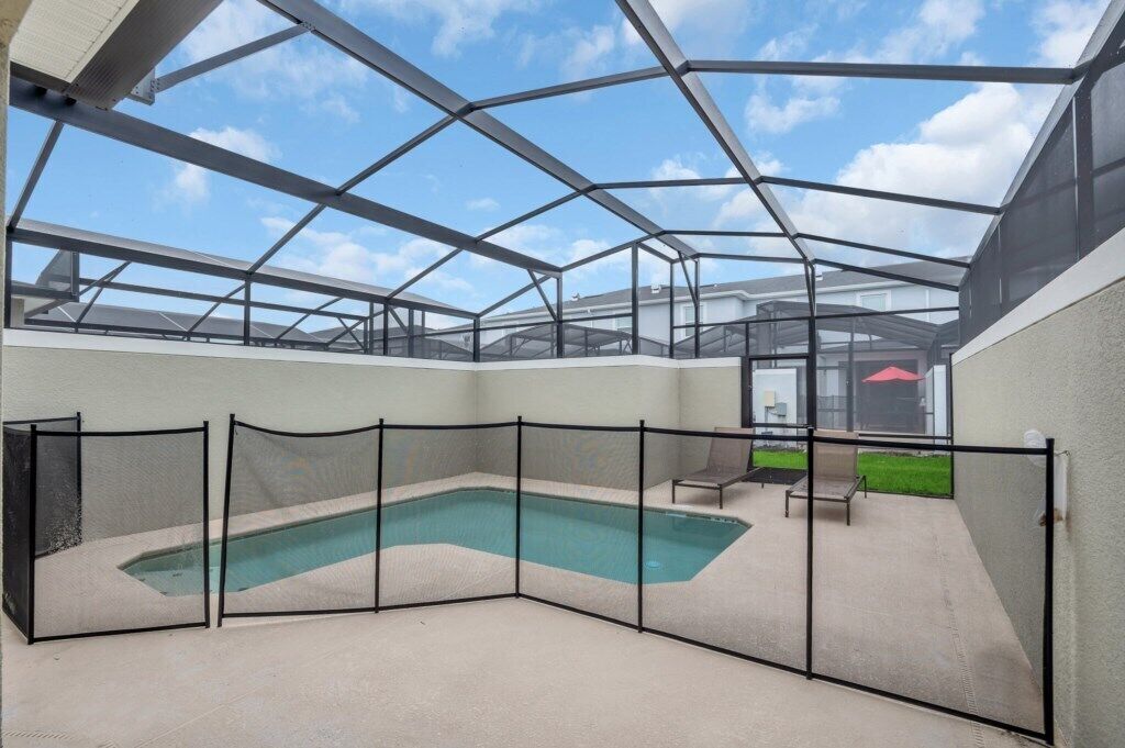 Ein überdachter Außenpool mit Glasdach, umgeben von einem schwarzen Zaun und einer Terrasse mit Stühlen.