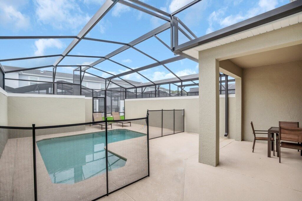Una piscina exterior cubierta con techo de cristal, rodeada por una valla, y una mesa con sillas.
