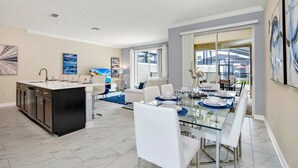 A modern kitchen with a central island, a dining area with a glass table, and a living space with a sofa and coffee table. - Story Lake Town Home  With Pool (Kissimmee)