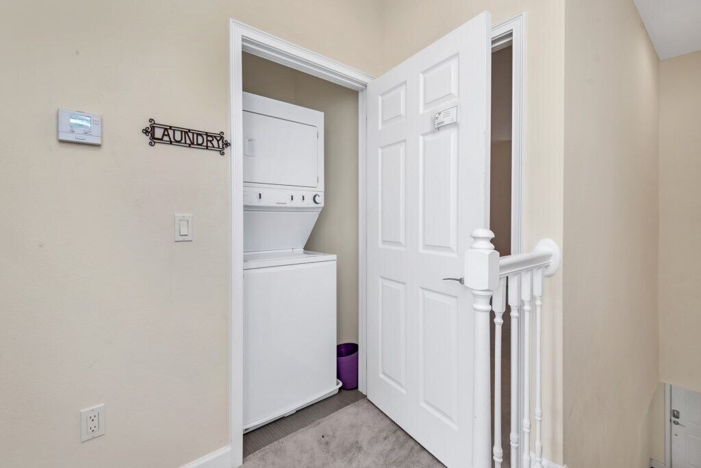 A laundry room with a white washer and dryer, a purple trash bin, and a sign that reads "LAUNDRY".
