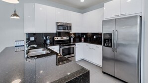 A modern kitchen with white cabinets, stainless steel appliances, and a granite countertop. - 3 bed Modern Town Home On a Luxury Development Close to Disney (Clermont)