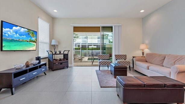 A modern living room with a flat-screen TV, a sofa, a coffee table, and a TV stand. - 3 bed Modern Town Home On a Luxury Development Close to Disney (Clermont)