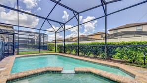 Una piscina con cerramiento de vidrio, rodeada por un borde de ladrillo y un seto.