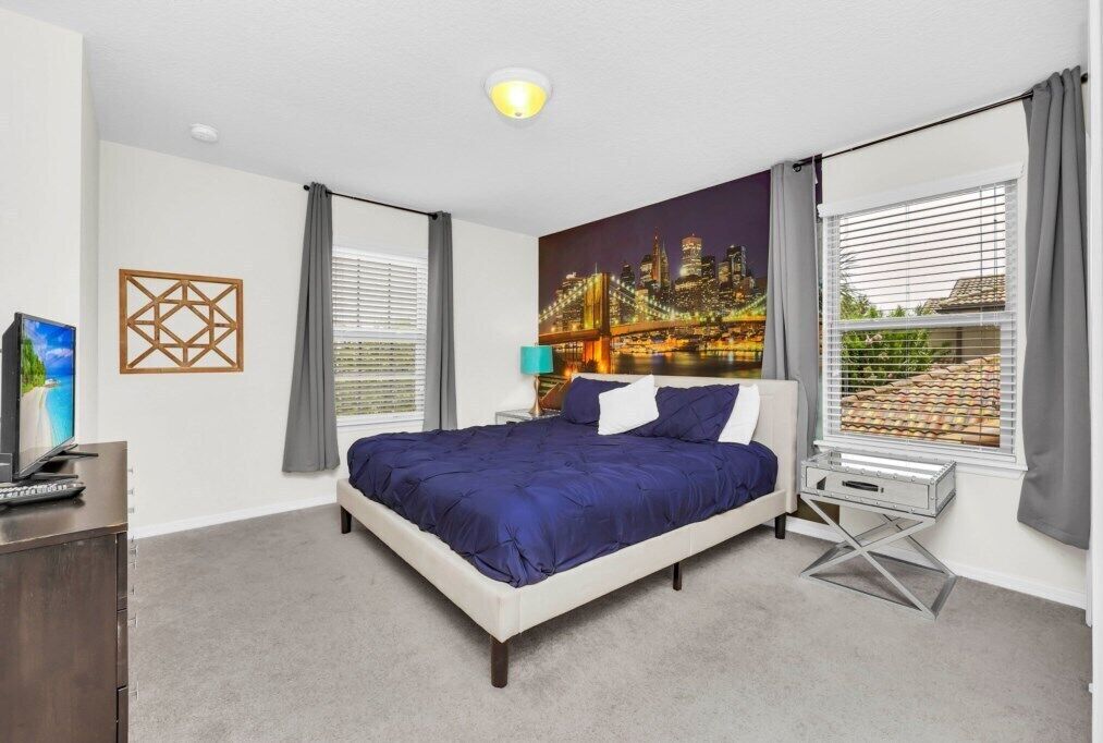A bedroom with a large bed, a cityscape mural, a TV, and a desk with a lamp.