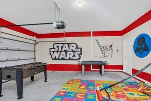 A room with a foosball table, a ping pong table, and Star Wars-themed decorations including a wall mural and a Star Wars character.