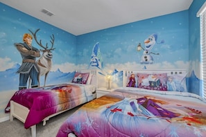 A bedroom with two beds, each with a themed bedspread, and a mural on the wall depicting characters from a winter-themed movie.