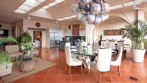 Amplia sala de estar con mesa de comedor de vidrio, sillas blancas y una lámpara moderna.