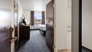 Une chambre d’hôtel avec un lit, un bureau avec une lampe, une fenêtre avec des rideaux et une vue sur l’extérieur.