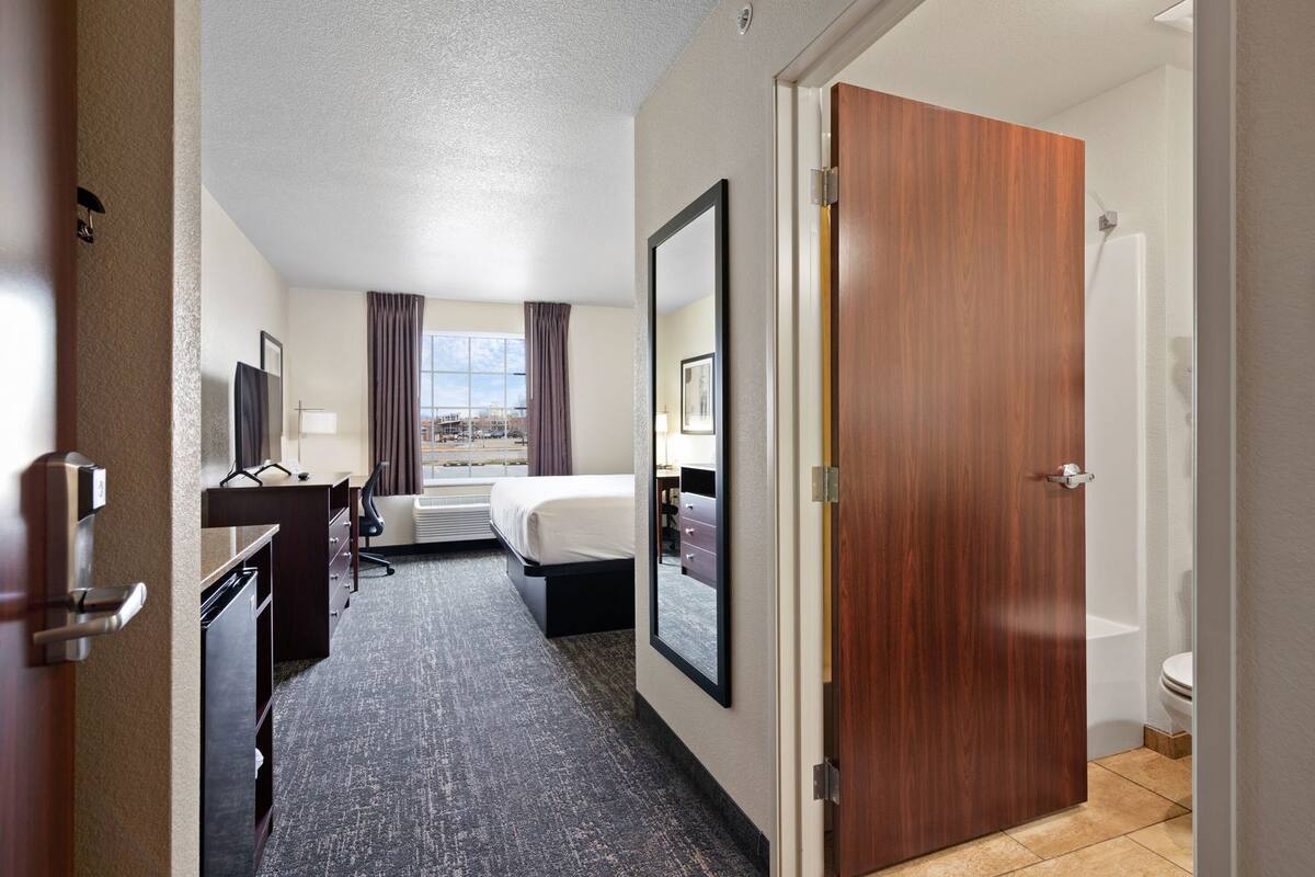 A hotel room with a bed, desk, chair, and a view of the outside.