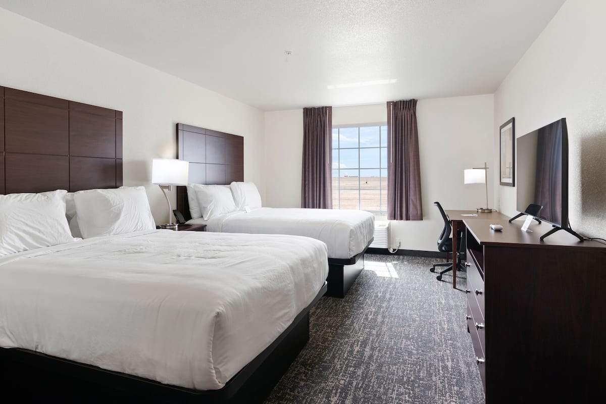 A hotel room with two beds, a desk, a chair, a lamp, and a large window with curtains.
