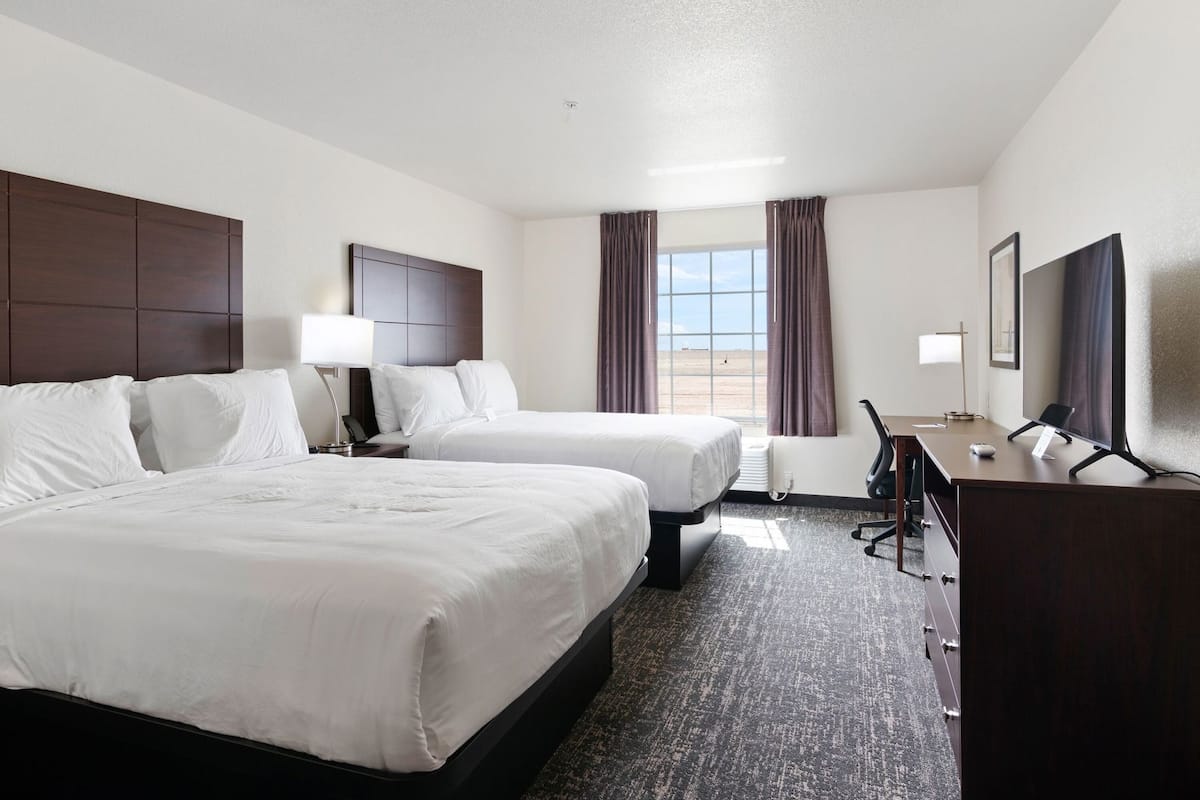 A hotel room with two beds, a desk, a chair, a TV, and a window with curtains.
