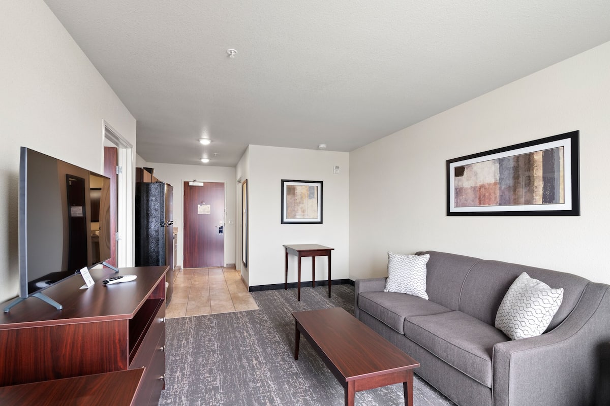 A modern living room with a sofa, coffee table, and a TV. There is a hallway leading to other rooms.