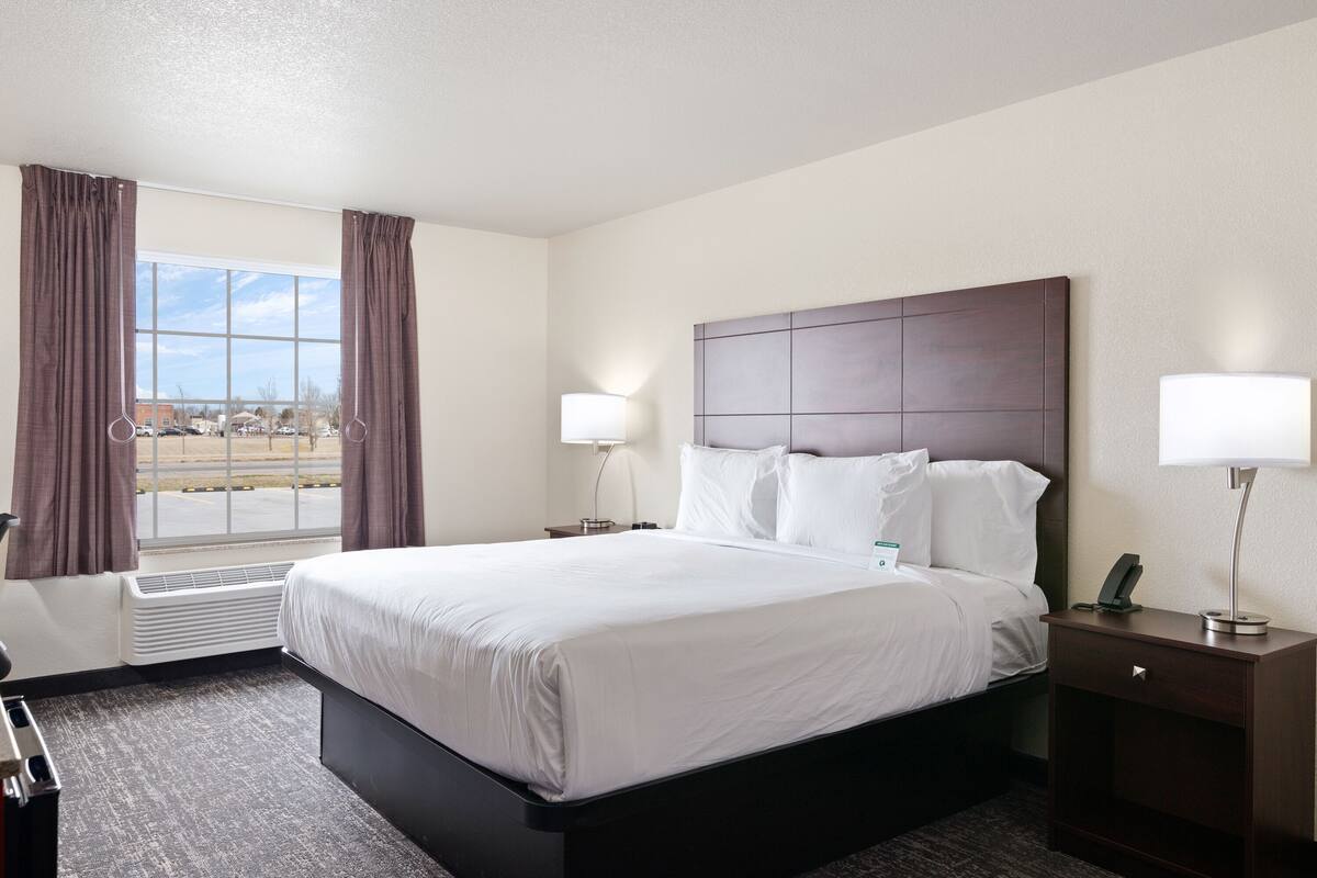 A hotel room with a large bed, two bedside lamps, a nightstand, and a window with curtains.