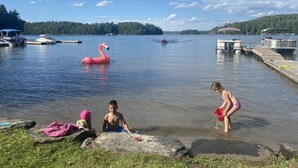 A lake with boats, a pink flamingo float, and people near the water's edge. - 3 BEDROOM LAKE FRONT COTTAGE WITH SPECTACULAR LAKE VIEWS AND SERENE ATMOSPHERE (Utterson)
