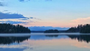 A calm lake with a forested shoreline and a clear sky. - 3 BEDROOM LAKE FRONT COTTAGE WITH SPECTACULAR LAKE VIEWS AND SERENE ATMOSPHERE (Utterson)