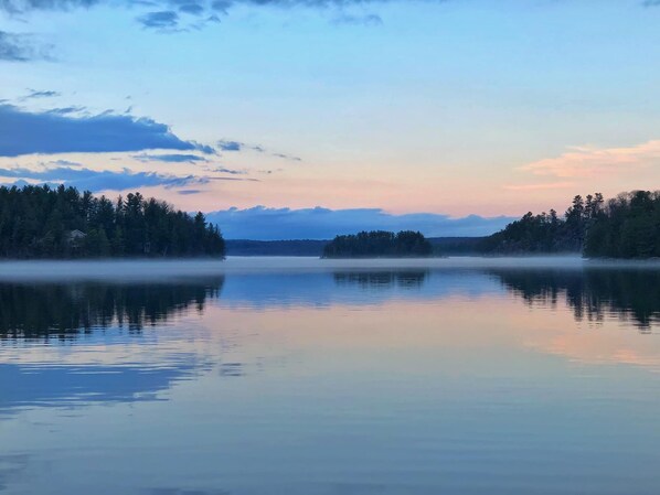 Tyyni järvi, jonka rannalla on metsää ja jonka yllä on kirkas taivas.