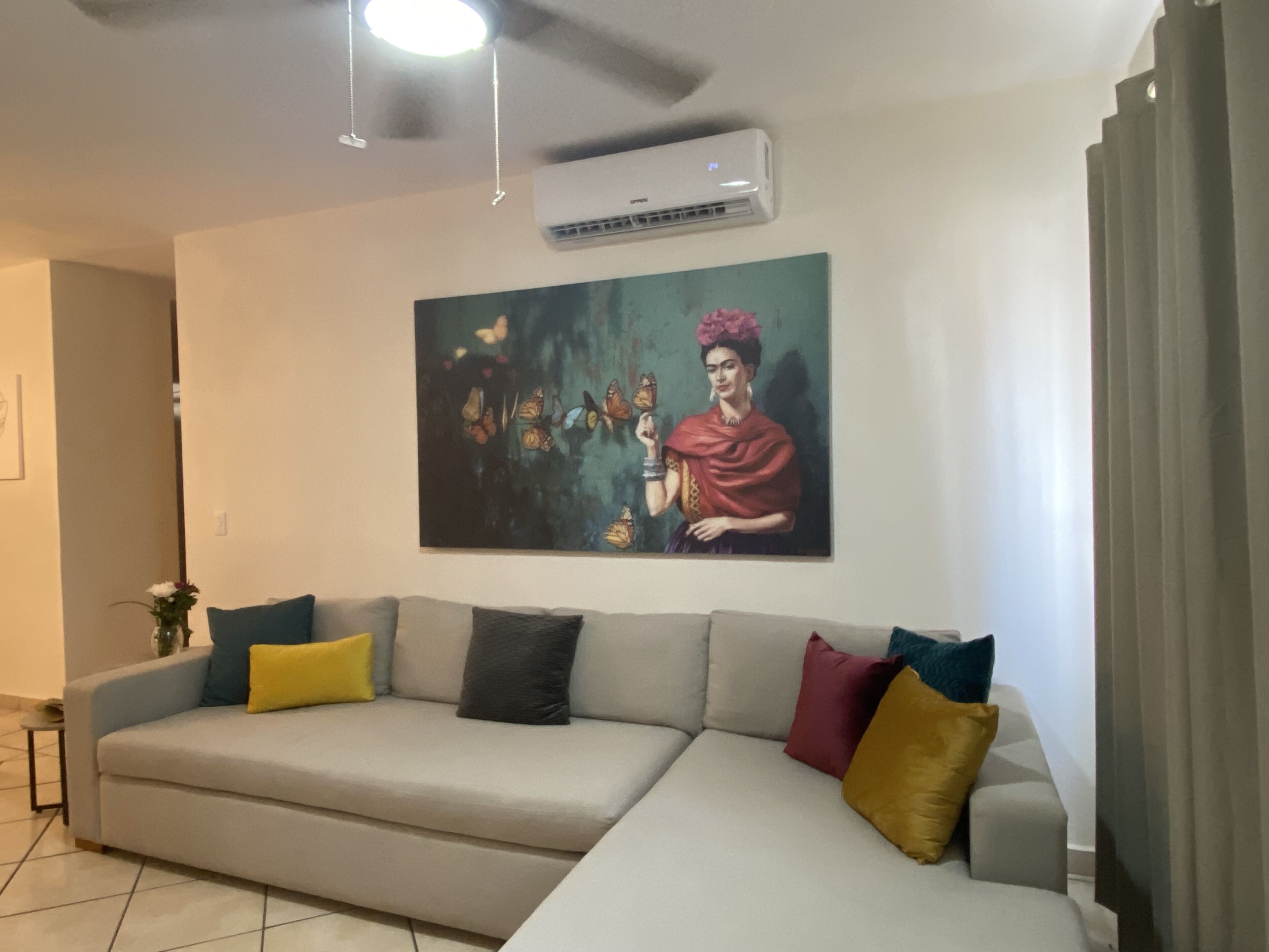 Un soggiorno con un divano grigio, cuscini colorati, una ventola a soffitto e un condizionatore d'aria a parete.