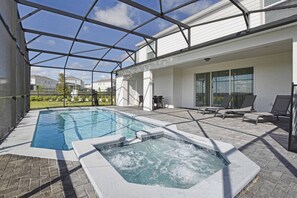 A covered outdoor swimming pool area with a hot tub, lounge chairs, and a view of neighboring houses.