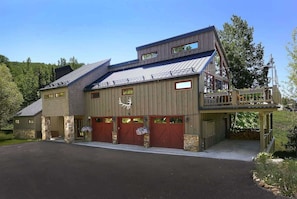 A large, multi-story building with a prominent balcony, stone pillars, and a garage with red doors.