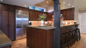 Una cocina moderna con armarios de madera, un refrigerador de acero inoxidable, una isla central con taburetes e iluminación empotrada en el techo.