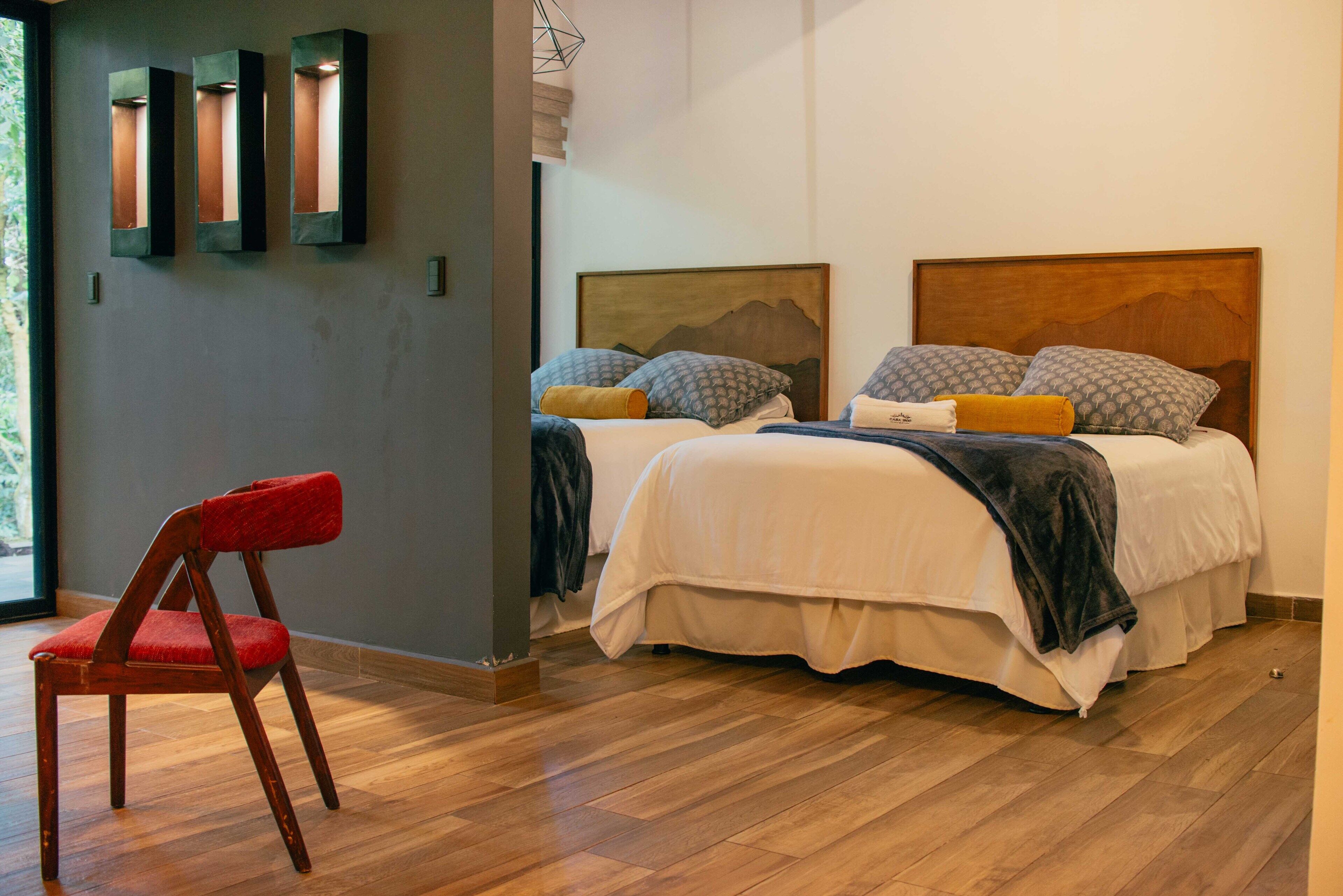 Une chambre moderne avec deux lits, un fauteuil rouge et un plancher en bois.