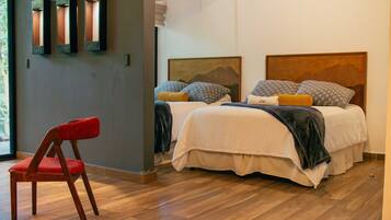 A modern bedroom with two beds, a red chair, and a wooden floor.
