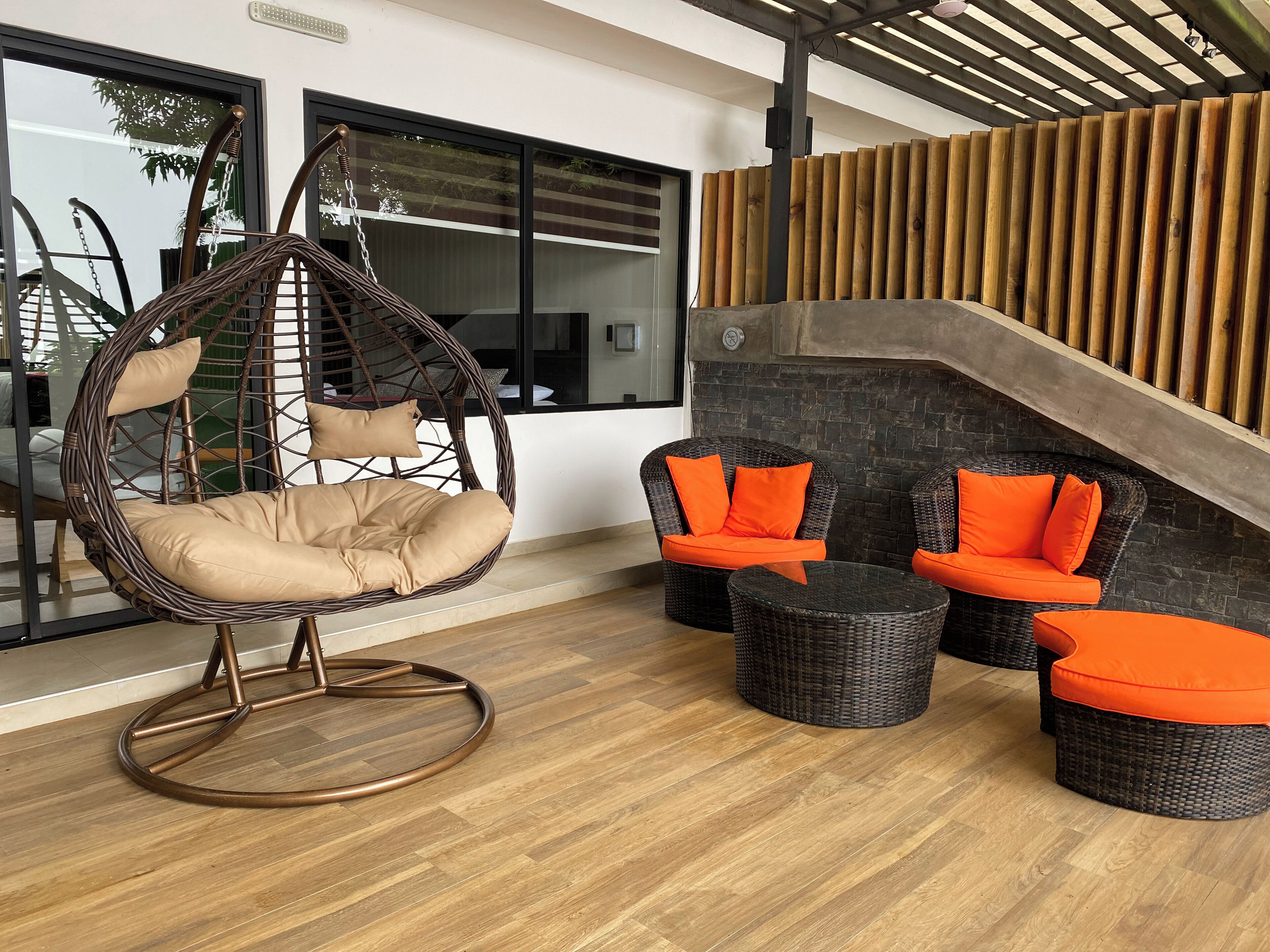 A modern outdoor seating area with a hanging chair, wicker sofas, and a stone wall.