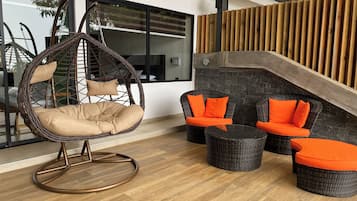 A modern outdoor seating area with a hanging chair, wicker sofas, and a stone wall.