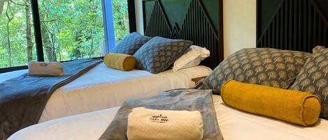 A hotel room with two beds, a large window with a view of trees, and a geometric-patterned headboard.