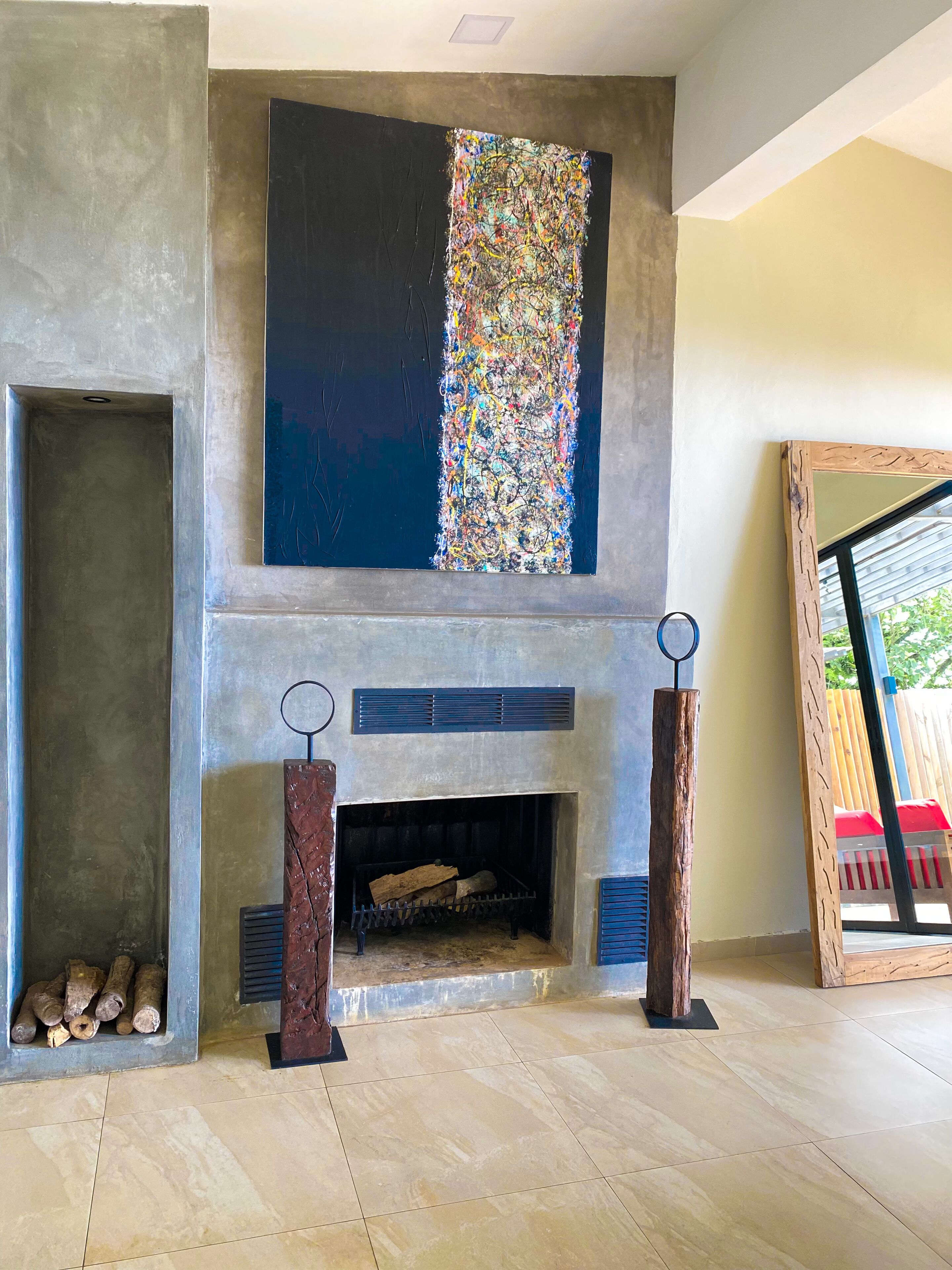 A modern living room with a fireplace, a large abstract painting, and a wooden-framed mirror.
