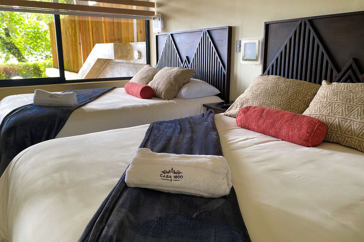 Habitación de hotel con dos camas, cada una con cabecera, almohadas y una toalla doblada sobre la cama.