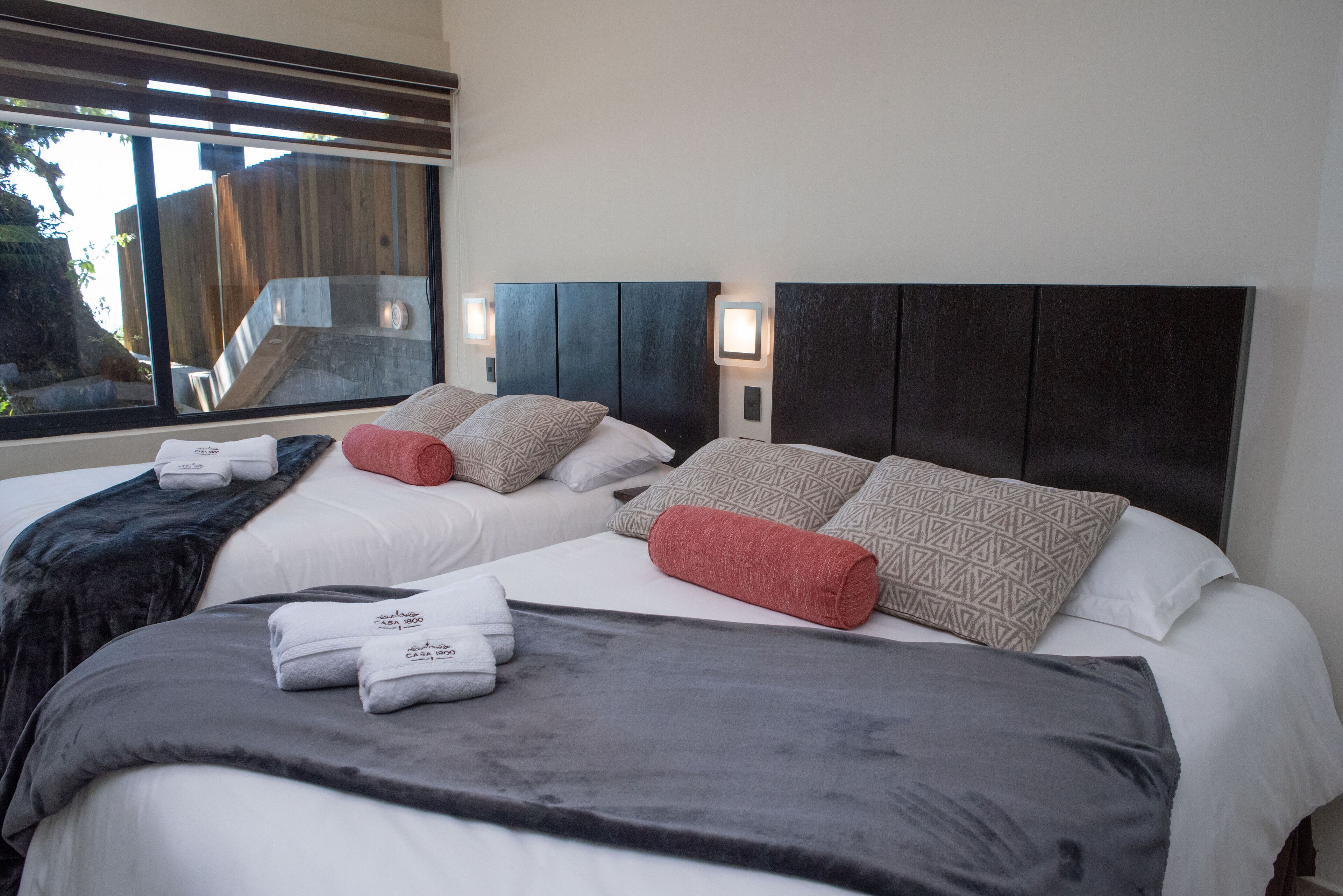 A hotel room with two beds, a large window, and a view of a wooden deck.