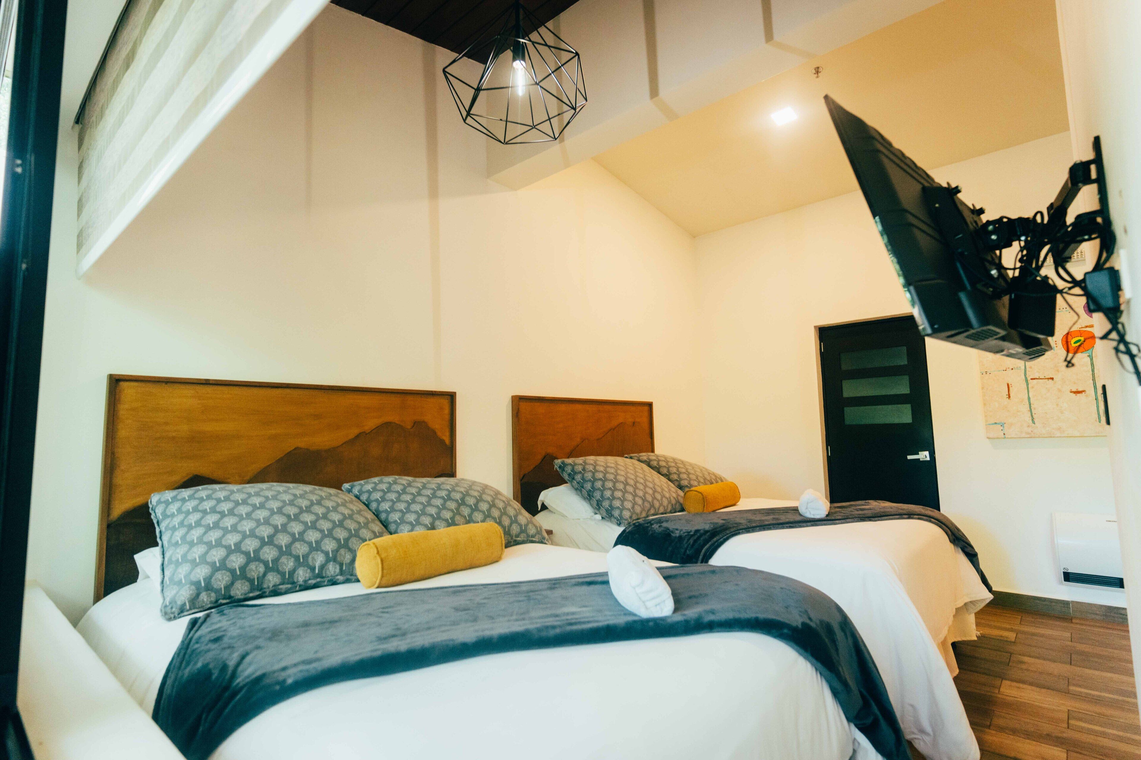 Een hotelkamer met twee bedden, houten hoofdeinden en een wandgemonteerde televisie.