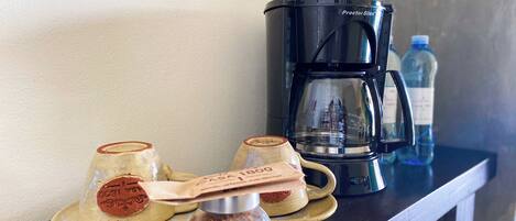 A coffee maker, two cups, and a spice jar on a counter.