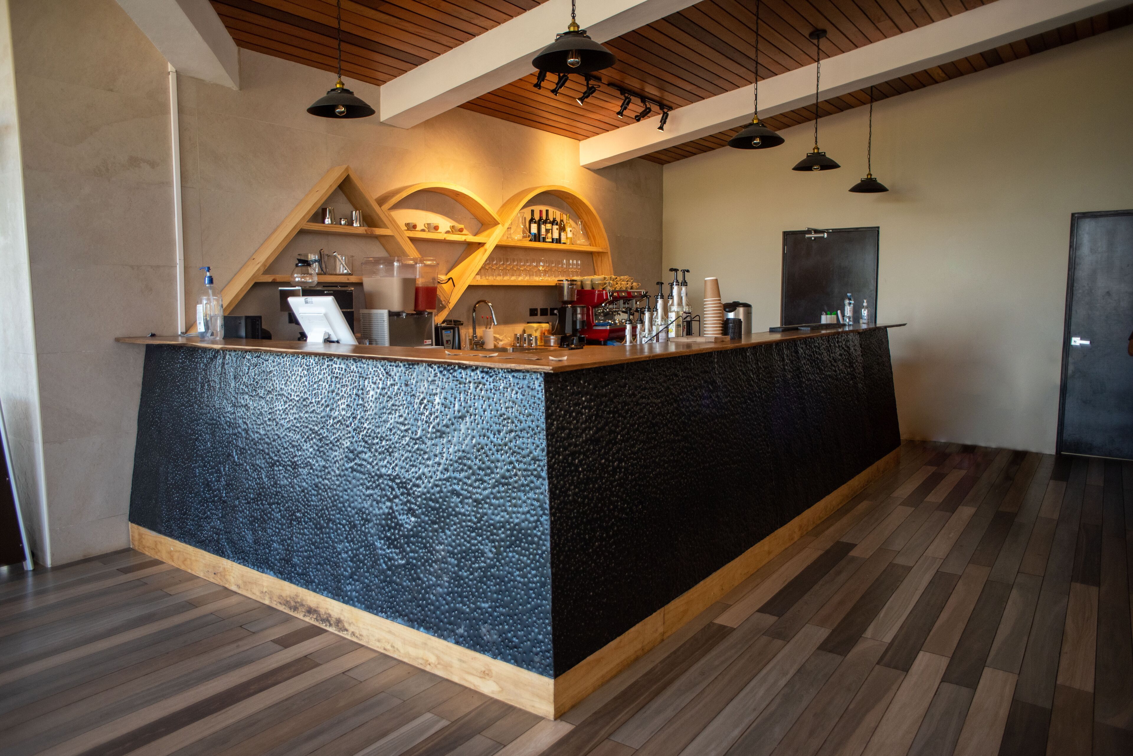 Una zona de bar con mostrador de madera, estantes con botellas y una máquina de café.