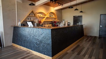 Uma área de bar com balcão de madeira, prateleiras com garrafas e uma máquina de café.