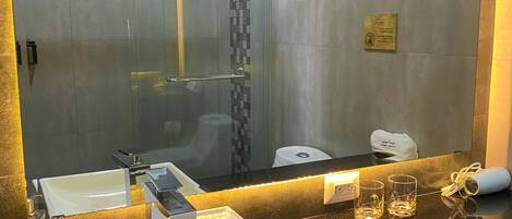 A modern bathroom with a large mirror, a white sink, and a glass shower enclosure.