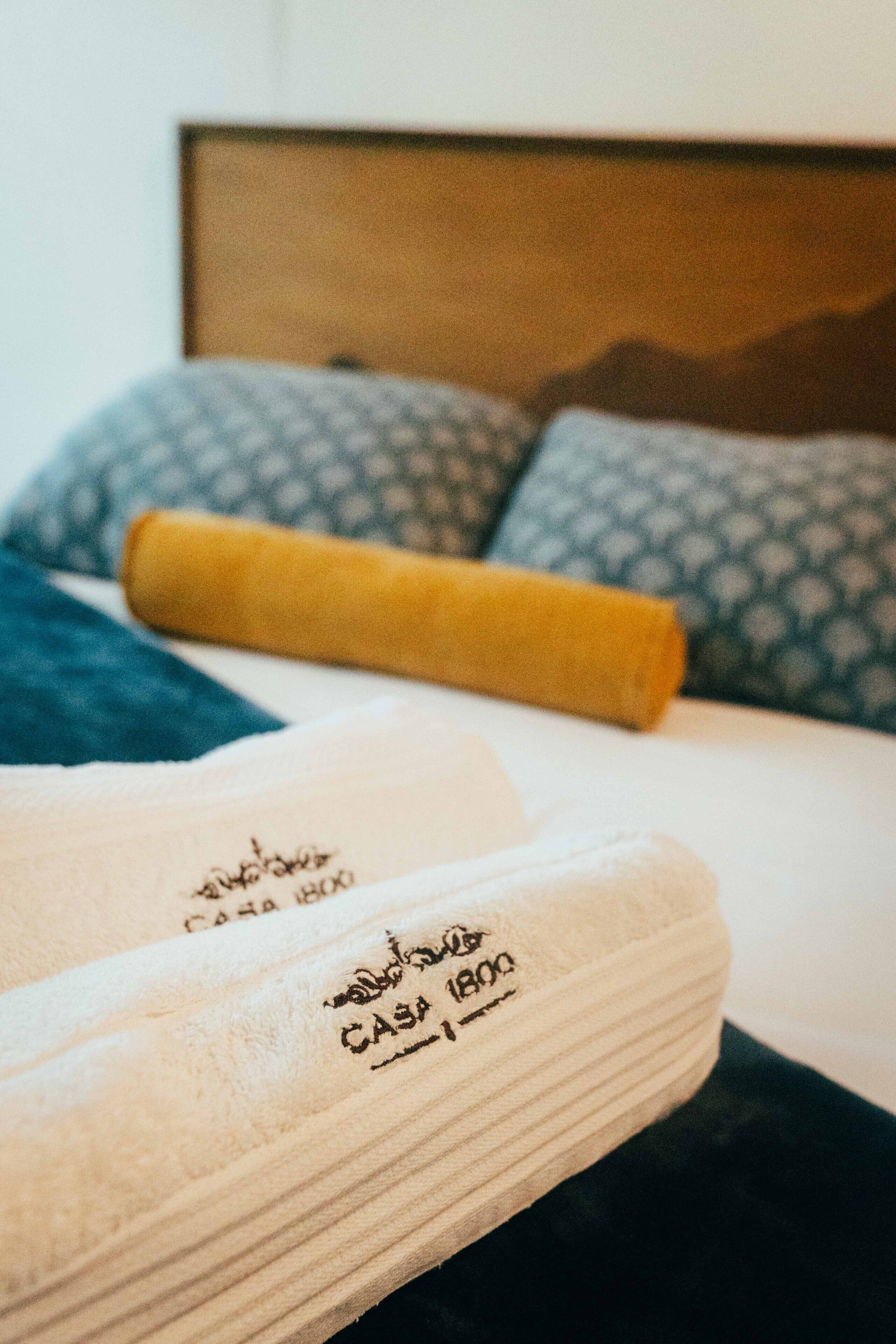 Una cama bien hecha con almohadas estampadas y una toalla enrollada.