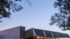 Un edificio moderno con fachada de vidrio, zona de estar al aire libre y un jardín con diversas plantas.