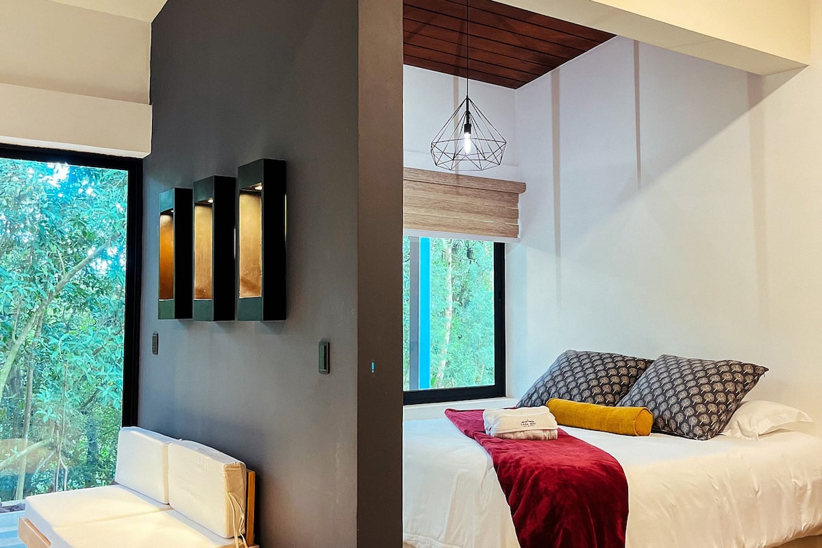 Un dormitorio moderno con una cama, un banco y un ventanal grande.
