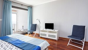 A bedroom with a bed, two chairs, a TV on a white cabinet, and a window with curtains. - Home2Book SeaFront Studio Punta del Hidalgo (Punta del Hidalgo)
