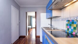 A narrow hallway leading to a kitchen with a modern stove, blue cabinets, and a patterned backsplash. - Home2Book SeaFront Studio Punta del Hidalgo (Punta del Hidalgo)