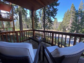 A wooden deck with two wicker chairs and a table, overlooking a forested area with a clear sky. - Mountain Chic Condo - Peaceful Family Home (Alpine Meadows)