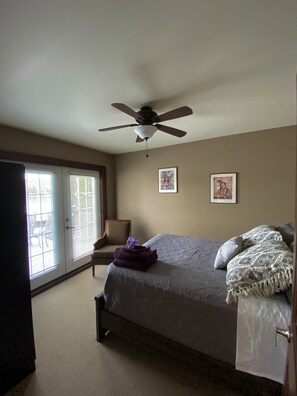 Une chambre à coucher avec un lit, un ventilateur de plafond, une chaise et deux tableaux encadrés accrochés au mur.