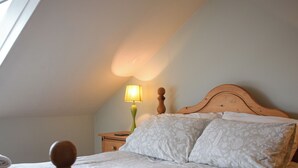 A bedroom with a sloped ceiling, a wooden headboard, a bedside lamp, and neatly folded towels on the bed. - This apartment has wonderful views over Bowness to Lake Windermere. (Bowness on Windermere)