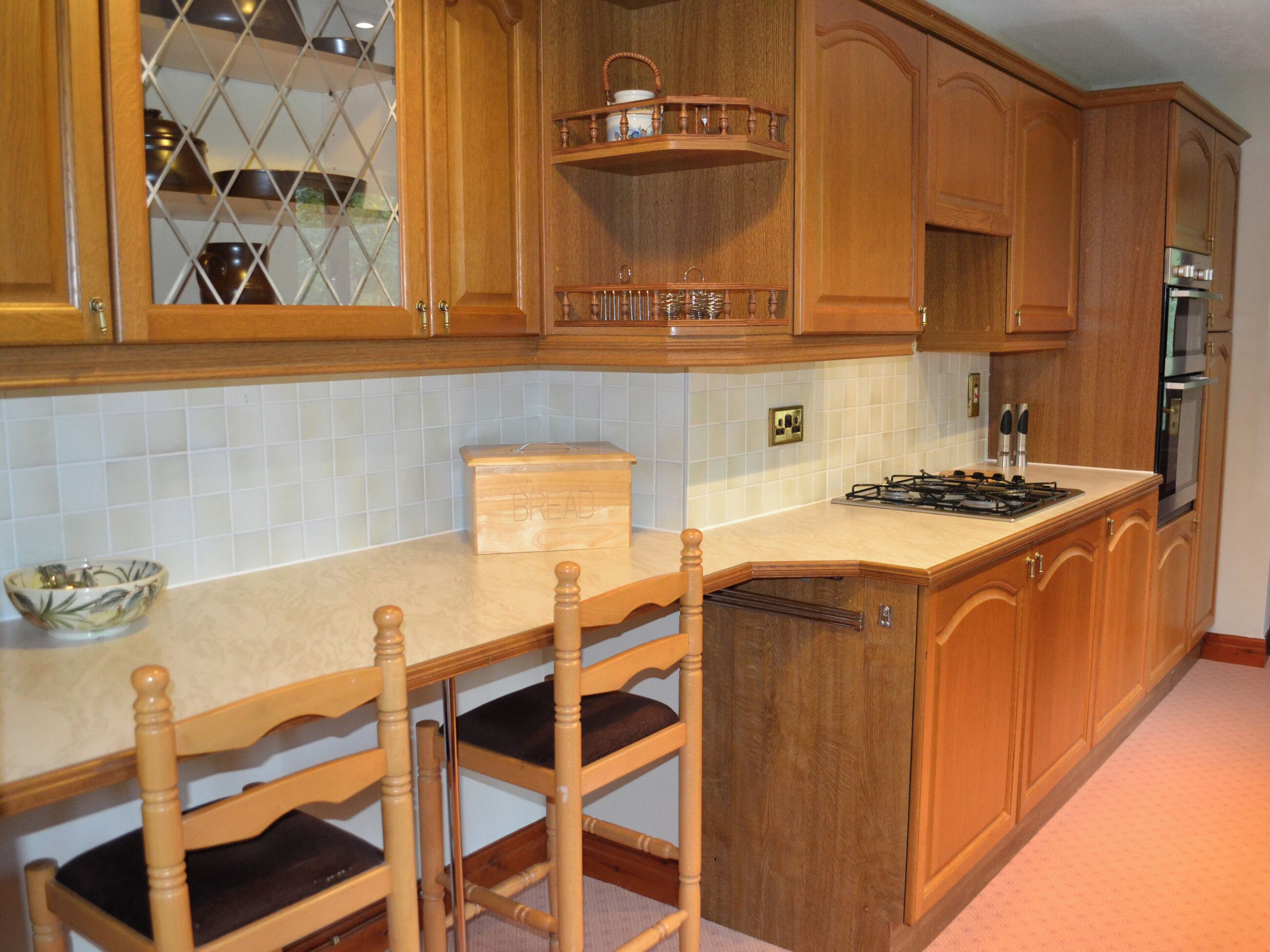A kitchen with wooden cabinets, a built-in stove, and a dining area with chairs.