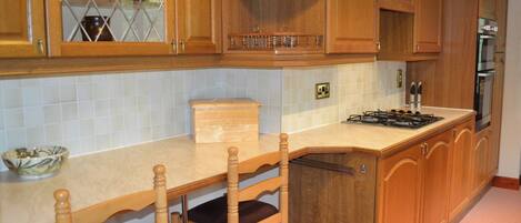 A kitchen with wooden cabinets, a built-in stove, and a dining area with chairs.